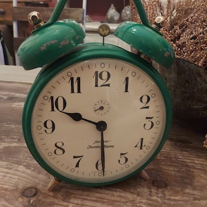 May include: A green vintage alarm clock with a white face and black hands. The clock has a Jerer Jumbo Alarm label and is made in Germany.