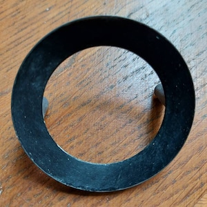 Puede incluir: Un anillo de goma negro con una superficie lisa y un borde ligeramente elevado. El anillo está diseñado para ajustarse alrededor de un objeto circular.