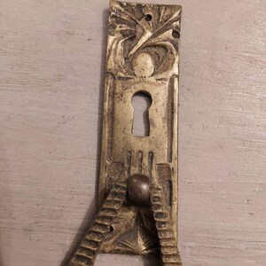Peut inclure: Une poignée de porte en laiton avec un design orné et un trou de serrure. La poignée a une boucle pour tirer la porte ouverte.