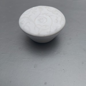 Op de afbeelding: Witte keramische knop met een reliëf bloemenpatroon.