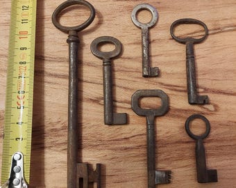 Puede incluir: Una colección de seis llaves antiguas, todas de metal y mostrando signos de edad y desgaste. Las llaves están dispuestas sobre una superficie de madera. Las llaves son de diferentes tamaños y formas, algunas con diseños intrincados.