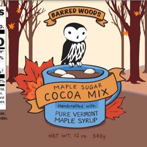 May include: A blue mug with a brown owl perched on the rim, filled with hot chocolate and marshmallows. The mug is surrounded by fall leaves and the text "Maple Sugar Cocoa Mix" is written in orange and brown. The text "Handcrafted with Pure Vermont Maple Syrup" is written in black below the mug. The product is a 12 ounce (340g) bag of maple sugar cocoa mix.
