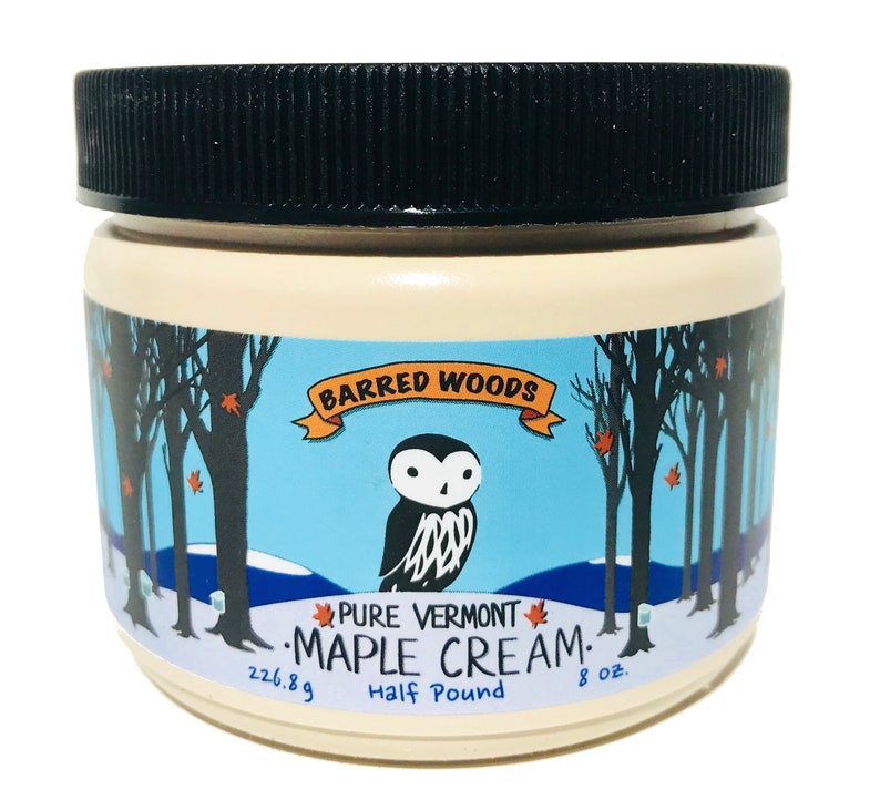 Może przedstawiać: Biały słoik z czarną pokrywką i etykietą z napisem "Barred Woods Pure Vermont Maple Cream. Half Pound 8 oz. 226.8g". Etykieta przedstawia kresk&oacute;wkową sowę i zimową scenę z drzewami i śniegiem.