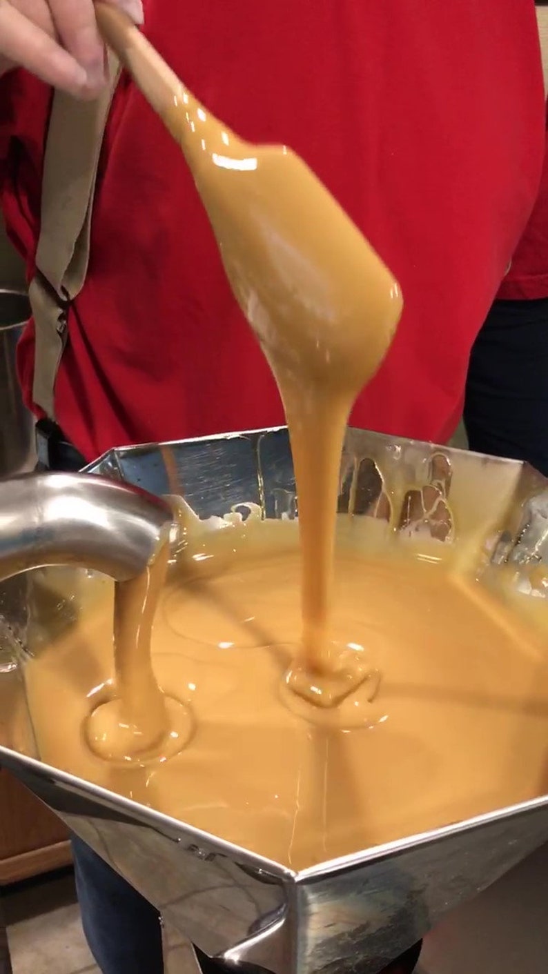 K&ouml;nnte beinhalten: Eine Person gie&szlig;t eine dicke, goldene Karamellsauce aus einem Holzl&ouml;ffel in eine Sch&uuml;ssel aus Edelstahl. Der Karamell ist glatt und gl&auml;nzend, und die Sch&uuml;ssel ist mit mehr Sauce gef&uuml;llt.