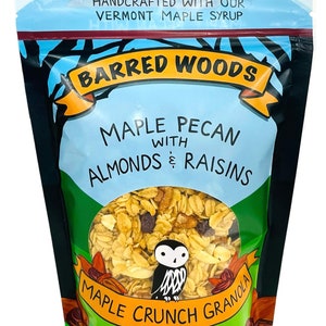 Puede incluir: Una bolsa de 284 g de granola Barred Woods Maple Crunch Granola con pecanas, almendras y pasas. La bolsa es negra con una etiqueta azul y amarilla que presenta un b&uacute;ho de dibujos animados. La granola es visible a trav&eacute;s de una ventana transparente en la bolsa.