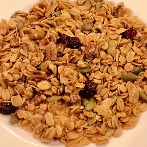 Puede incluir: Primer plano de un bol de granola con avena, nueces de pec&aacute;n, semillas de calabaza y ar&aacute;ndanos secos.