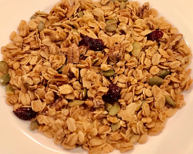Puede incluir: Primer plano de un bol de granola con avena, nueces de pec&aacute;n, semillas de calabaza y ar&aacute;ndanos secos.