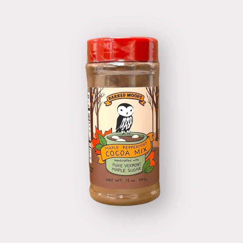 May include: A brown glass jar with a red lid containing maple peppermint cocoa mix. The label features a cartoon owl and the text "BARRED WOODS", "MAPLE PEPPERMINT COCOA MIX", "Handcrafted with PURE VERMONT MAPLE SUGAR", and "NET WT. 12 oz. 340g".