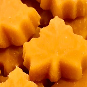 May include: A close-up of maple candies shaped like maple leaves. The candies are a light brown color and have a smooth, glossy finish.