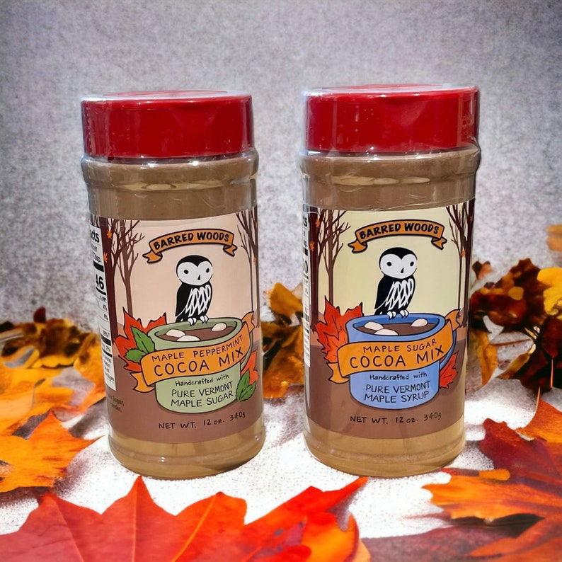 May include: Two 12-ounce jars of Barred Woods cocoa mix. The jar on the left is labeled "Maple Peppermint Cocoa Mix" and the jar on the right is labeled "Maple Sugar Cocoa Mix". Both jars feature an owl illustration and are handcrafted with pure Vermont maple syrup or sugar.