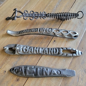 May include: Four vintage metal bottle openers with embossed text. The openers are in various shapes and designs, including one with a spring coil and the words "CARROLL". Other openers have the words "SOUVENIR", "GARLAND", and "AETNA".
