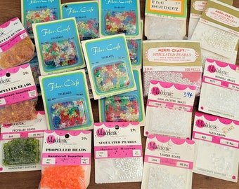 May include: Assortment of colorful and clear plastic beads in various shapes and sizes, including propeller, rondelle, saucer, and simulated pearls. The beads are packaged in small plastic bags with labels that include the bead type, size, and quantity. The bags are arranged on a wooden surface.