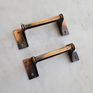 May include: Two antique-style door pulls with a copper finish. The pulls are made of metal and have a simple, rectangular design. Each pull has a rounded, cylindrical handle.