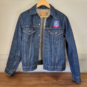 May include: A blue denim jacket with a patch on the left breast that says "Spirit of Skiing 76".