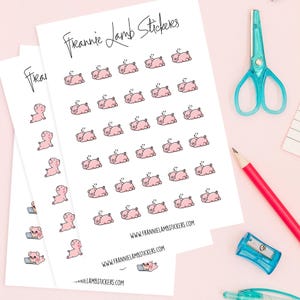 May include: Sheets of stickers featuring pink cartoon pigs in various poses, including sleeping and using a laptop. The stickers are labelled "Frannie Lamb Stickers" with a website address. A red pencil, blue scissors, and a pencil sharpener are also visible.