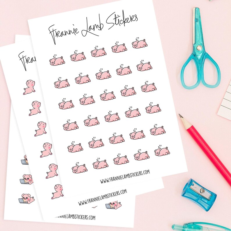May include: Sheets of stickers featuring pink cartoon pigs in various poses, including sleeping and using a laptop. The stickers are labelled "Frannie Lamb Stickers" with a website address. A red pencil, blue scissors, and a pencil sharpener are also visible.