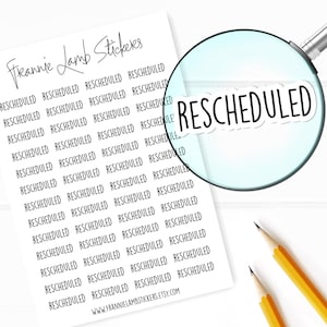 Puede incluir: Una hoja de papel blanco con el texto "Freanie Lamb Stickers" en la parte superior. El papel está cubierto de texto negro que dice "RESCHEDULED" repetido muchas veces. Una lupa está sobre el texto, enfocando una de las palabras "RESCHEDULED". Dos lápices amarillos están sobre la superficie blanca junto al papel.