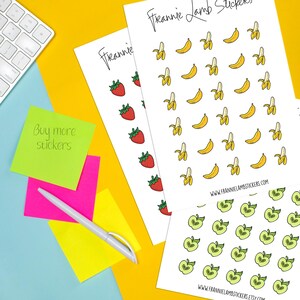 K&ouml;nnte beinhalten: Bl&auml;tter mit Aufklebern mit Illustrationen von Erdbeeren, Bananen und &Auml;pfeln. Die Aufkleber befinden sich auf wei&szlig;em Papier, mit dem Markennamen "Frannie Lamb Stickers" oben und unten. Ein Stift und Haftnotizen sind ebenfalls im Bild.