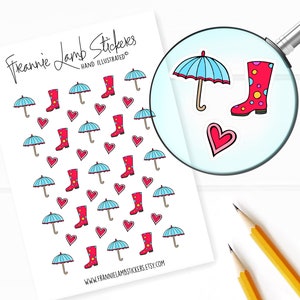 Puede incluir: Una hoja de pegatinas con un patrón repetitivo de botas de lluvia rojas, paraguas azules y corazones rosas. El texto "Frannie Lamb Stickers" y "Hand Illustrated" está en la parte superior de la hoja. La hoja está sobre una superficie blanca con dos lápices amarillos.