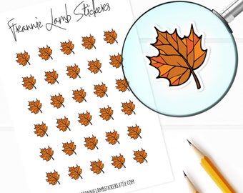 May include: A sheet of stickers featuring a repeating pattern of orange and brown maple leaves. The sheet is white with the text "Frannie Lamb Stickers" at the top and "www.frannielambstickers.etsy.com" at the bottom. A magnifying glass shows a close-up of a single sticker with a larger maple leaf.