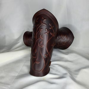Puede incluir: Un par de protectores de brazo de cuero marrón oscuro con un diseño en relieve de hojas y vides. Los protectores de brazo cilíndricos tienen una parte superior acampanada. Para disfraces o recreaciones históricas.