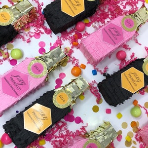 Puede incluir: Una colección de ocho piñatas de fiesta en forma de botellas de champán, negras y rosas. Cada piñata tiene una etiqueta dorada con el texto "JRG PROSECCO" y "EXCEEDING EXPECTATIONS". Las piñatas están decoradas con purpurina dorada y el año "2019".