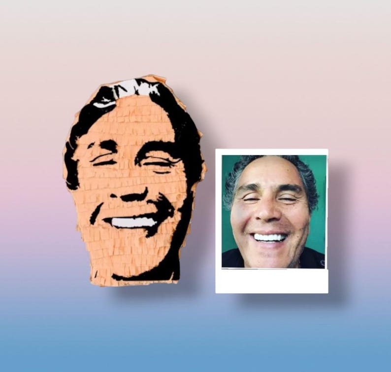 May include: A peach-colored pi&ntilde;ata shaped like a human head with black graphic facial features and a smiling expression, displayed alongside a square photograph of a person with a similar smiling face against a solid green background.