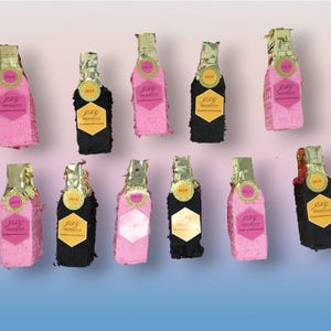 May include: A collection of pink and black piñata bottles with gold foil tops. Each bottle features a label reading "JRG Prosecco" and the year "2019". The piñatas are displayed against a pink and blue gradient background.