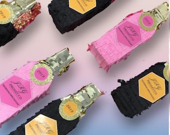May include: An overhead shot of several champagne bottle-shaped piñatas. The piñatas are in black and pink, with gold foil wrapping the top. Each bottle has a label that reads "JRG Prosecco" and the year "2019".