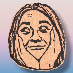 May include: A light-colored wooden slice featuring a black ink illustration of a person with long hair, eyes closed, and hands pressed against their cheeks. The wood grain is visible beneath the bold, dark lines of the portrait design.