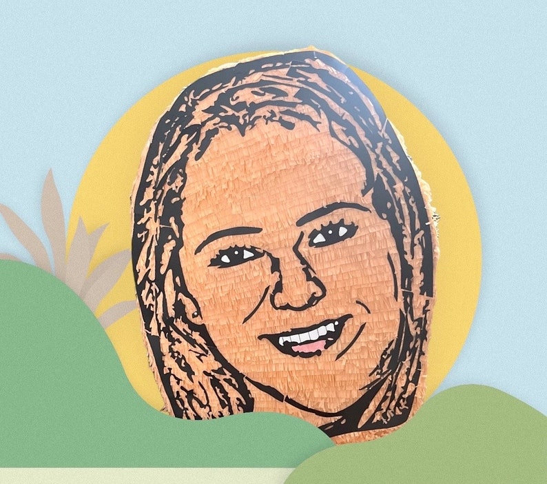 May include: A custom pi&ntilde;ata featuring a detailed black line art portrait of a person with long hair and a smiling expression. The portrait is rendered on a textured, light brown paper surface, capturing facial features including eyes, nose, and teeth.
