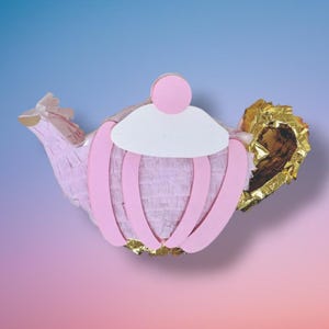 May include: A pink teapot piñata with a white and pink design. The teapot has a gold-colored handle and spout. The piñata is made of paper and cardboard.