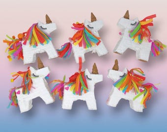 May include: Six white unicorn piñatas with rainbow manes and tails, brown horns, and closed eyes. Each piñata has a heart on its side. The piñatas are arranged on a gradient background of pink and blue.