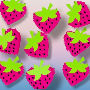 Puede incluir: Nueve decoraciones rosas en forma de fresa con hojas verdes y semillas negras están dispuestas sobre un fondo degradado. Las fresas son de un color rosa vibrante y las hojas de un verde brillante.
