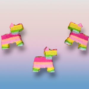 May include: Three colorful dog-shaped piñatas. Each piñata is made of layered paper in shades of pink, yellow, green, and orange. The piñatas are set against a gradient background of blue, pink, and white.