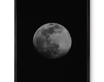 Op de afbeelding: Een ingelijste wandkunstprint met een contrastrijke, gedetailleerde zwart-witfoto van de maan, gecentreerd tegen een effen zwarte achtergrond. De maan toont zichtbare kraters en maanoppervlaktexturen in grijstinten.