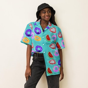 Puede incluir: Una camisa turquesa con un estampado de flotadores inflables y rodajas de sandía. La camisa tiene mangas cortas y un cuello clásico. El diseño incluye varios colores como morado, naranja, rojo y rosa.