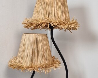 May include: A black metal table lamp with two woven straw lampshades. The lamp has a unique curved design and a square base.
