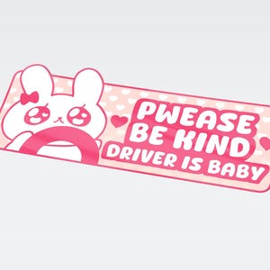 Peut inclure: Un autocollant rectangulaire rose avec un lapin mignon conduisant une voiture. Le texte "PWEASE BE KIND DRIVER IS BABY" est en rose et blanc. Le fond est rose clair avec de petits cœurs blancs.