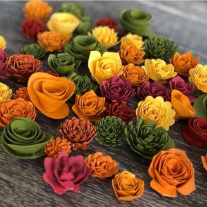 May include: A collection of paper flowers in various shades of orange, red, and green. The flowers are arranged in a random pattern on a wooden surface.