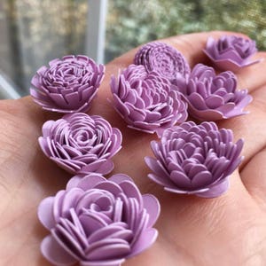May include: A collection of lavender paper flowers, each with a different size and shape. The flowers are arranged on a hand, showcasing their delicate details.