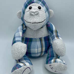 Puede incluir: Un mono de peluche azul y blanco a cuadros con pelaje gris. El mono tiene ojos negros y una sonrisa cosida. El juguete est&aacute; sentado sobre una superficie blanca.