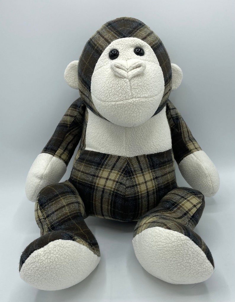 Puede incluir: Un mono de peluche con un patr&oacute;n de cuadros marrones y beige. El mono tiene pelaje blanco en la cara, las manos y los pies. El mono est&aacute; sentado con las piernas cruzadas.