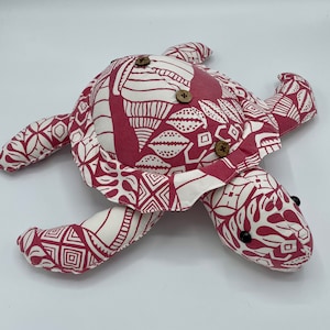 May include: A pink and white patterned fabric turtle with brown button eyes and wooden button accents.