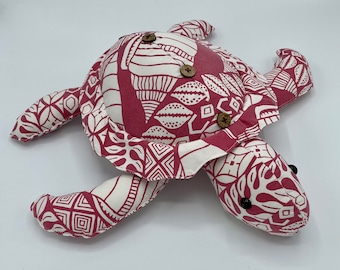 May include: A pink and white patterned fabric turtle with brown button eyes and wooden button accents.