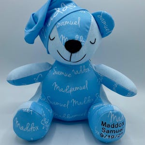 May include: A light blue teddy bear wearing a matching nightcap. The bear has the names "Samuel" and "Maddox" printed on it in white script. The bear's eyes are closed, and the date "9/19/21" is printed on the foot.