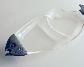 May include: Clear glass serving dish in the shape of a fish, with a silver-colored metal head and tail. The dish has a curved design and is likely used for serving appetizers or snacks. The fish-shaped design adds a unique touch.