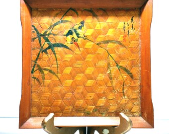 May include: Square bamboo tray with a woven geometric pattern and a painted bird and bamboo design. The tray has a dark brown wooden frame and is displayed on a gold-colored stand.