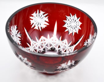 May include: A deep red glass bowl featuring intricate clear cut-glass starburst and snowflake patterns etched into the exterior surface. The bowl has a smooth, rounded rim and a polished finish, showcasing a contrast between the vibrant red glass and the clear, geometric, star-shaped engravings.