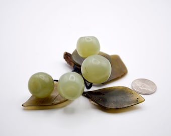 May include: A decorative arrangement of jade-colored spheres and leaf-shaped pieces. The spheres are round and smooth, with a pale green hue. The leaf pieces are a darker green and brown. A US quarter coin is included for size reference.